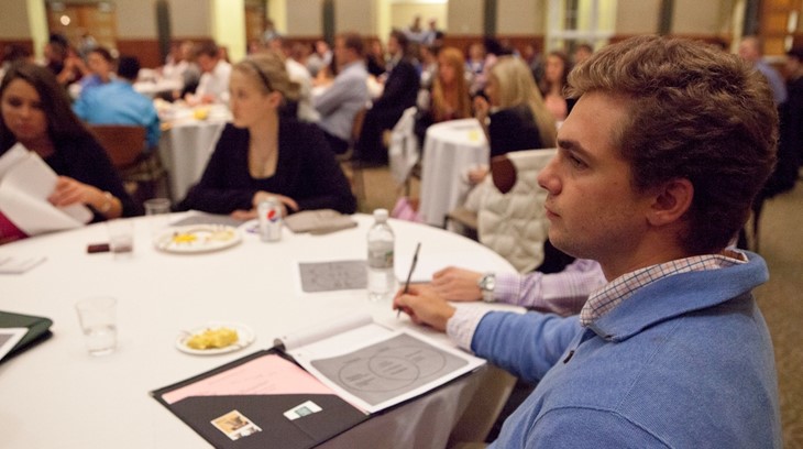 Business students sit at tables and listen during a presentation