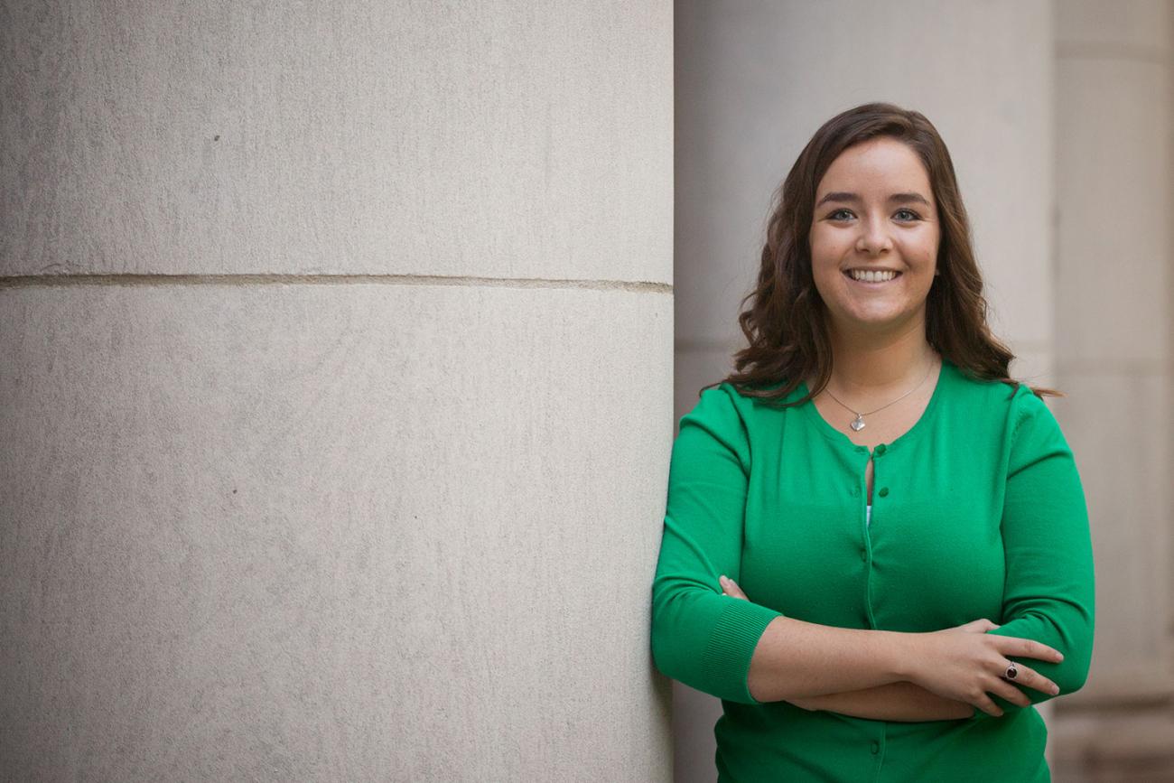 Smiling woman with brown hair in green shirt leaning against concrete column