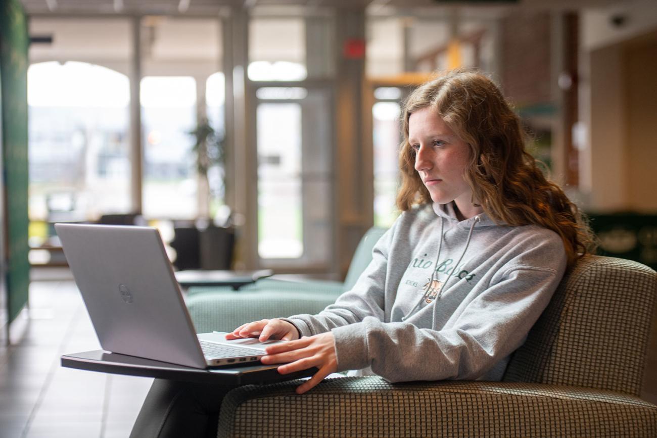 Girl at chair with laptop on tray in front of her