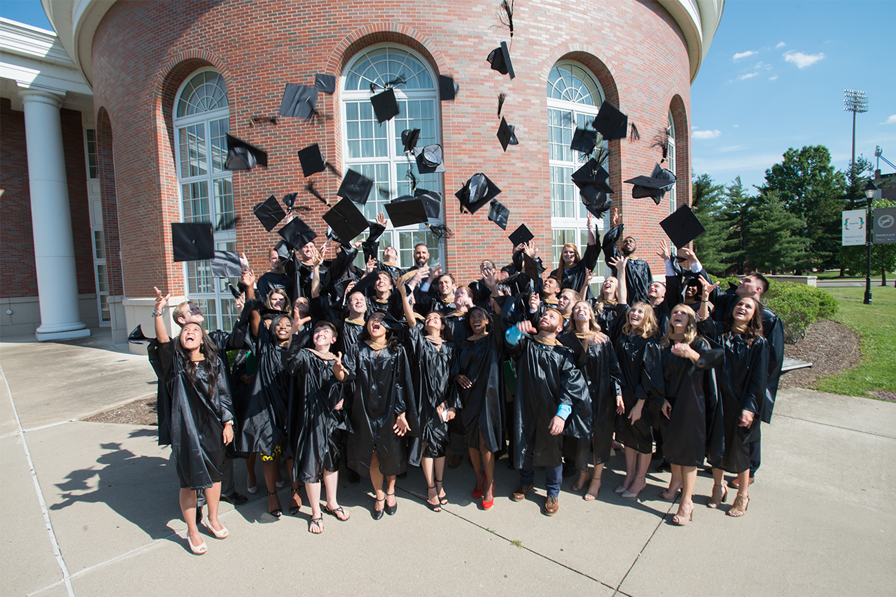 Graduates standing in front of red brick building throwing their caps up while smiling