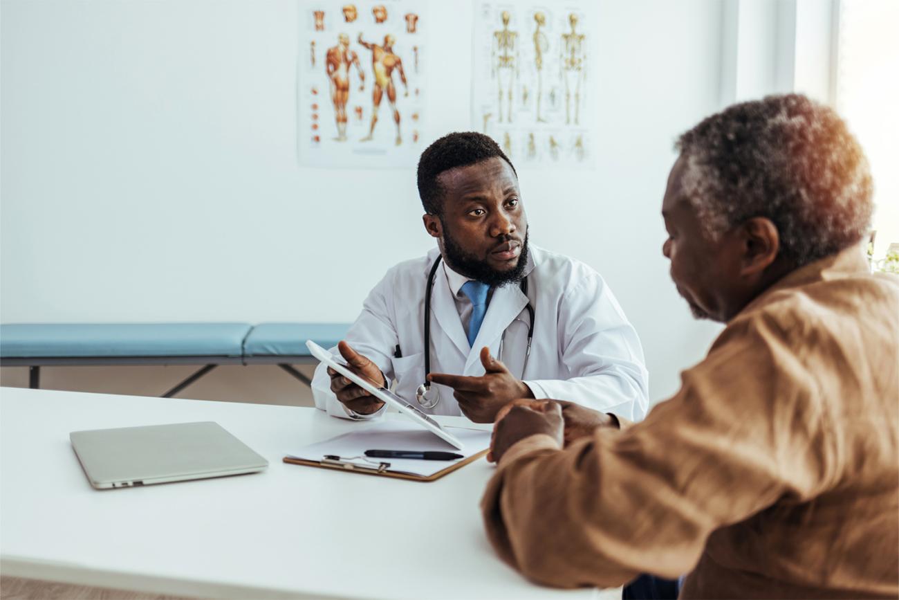 African American doctor sitting at table with patient in brown shirt