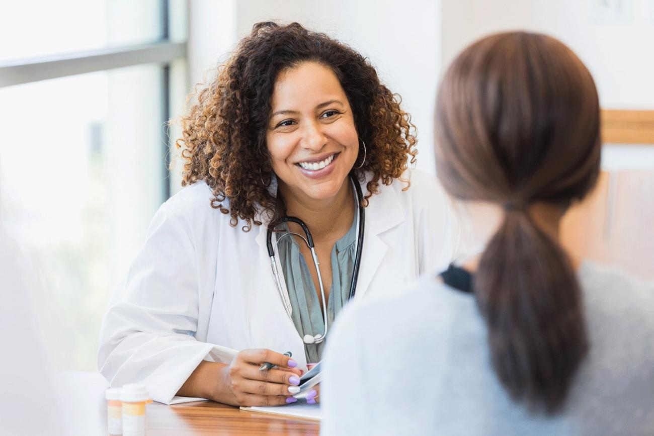 Smiling student of the online MSN Psychiatric Mental Health Nurse Practitioner program at a desk with a patient.