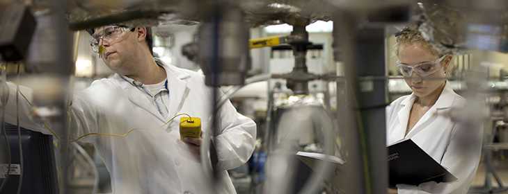 Two young researchers wearing lab coats using equipment