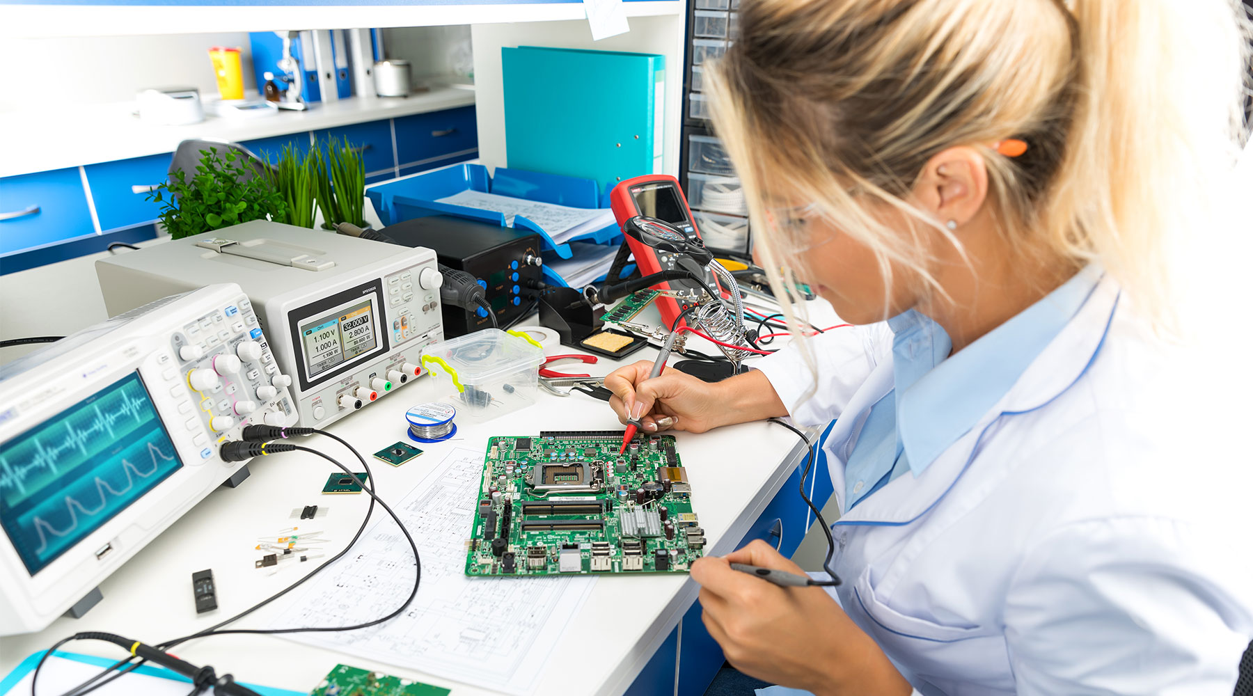 Female electrical engineer at work station testing circuits on board