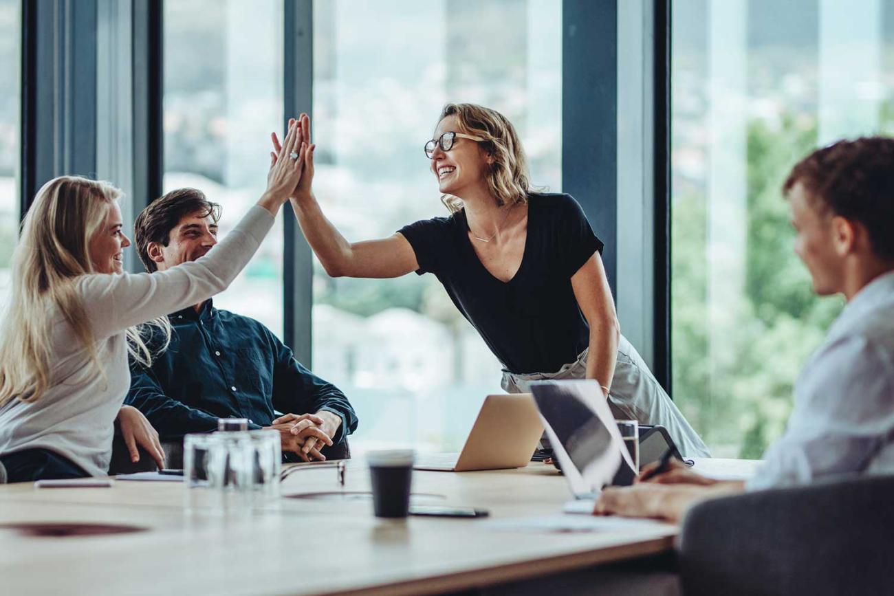 Group around table with woman standing to give a high five to student in six sigma black belt certificate program