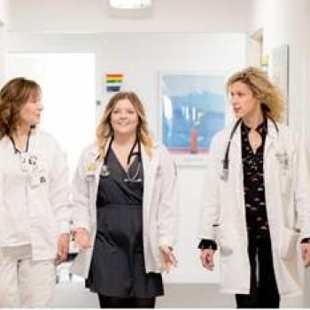 A group of three Heritage College students, wearing their white coats, walk down a hallway together.