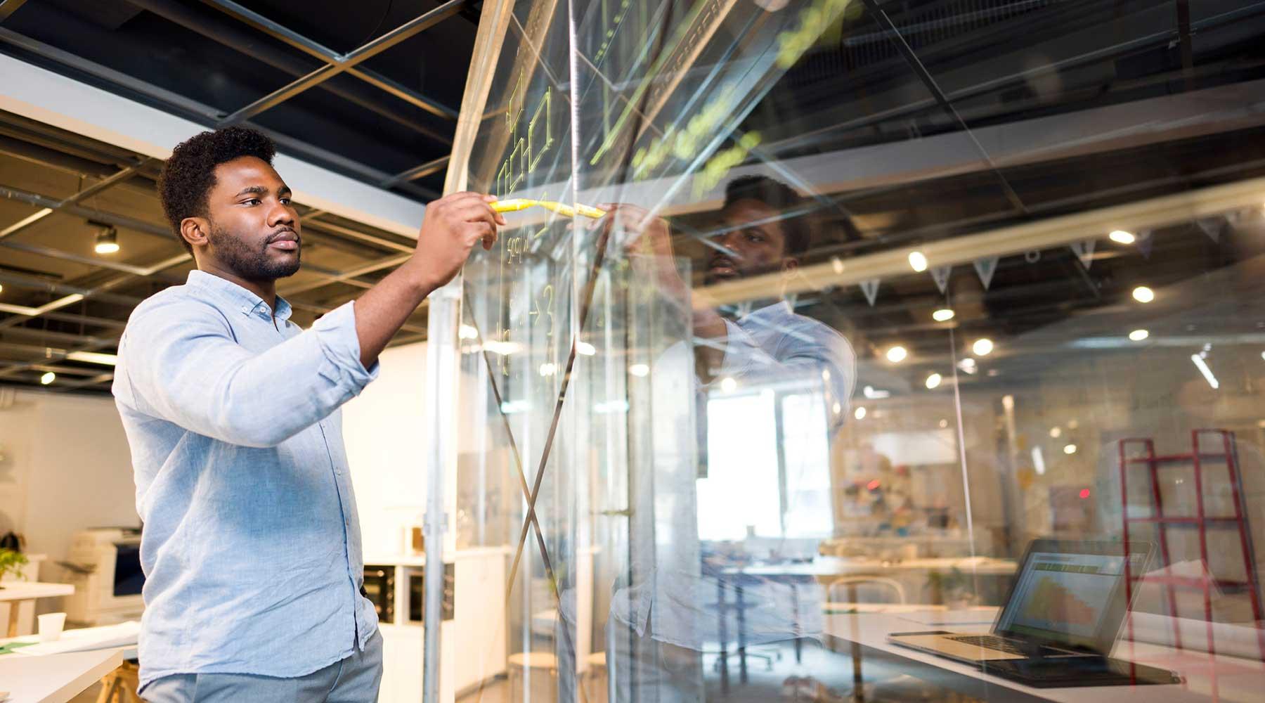 Man at glass board with marker utilizing a lean six sigma certificate to list equations