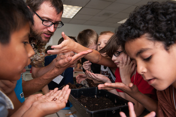 Children gather around bugs for inspection with the teacher