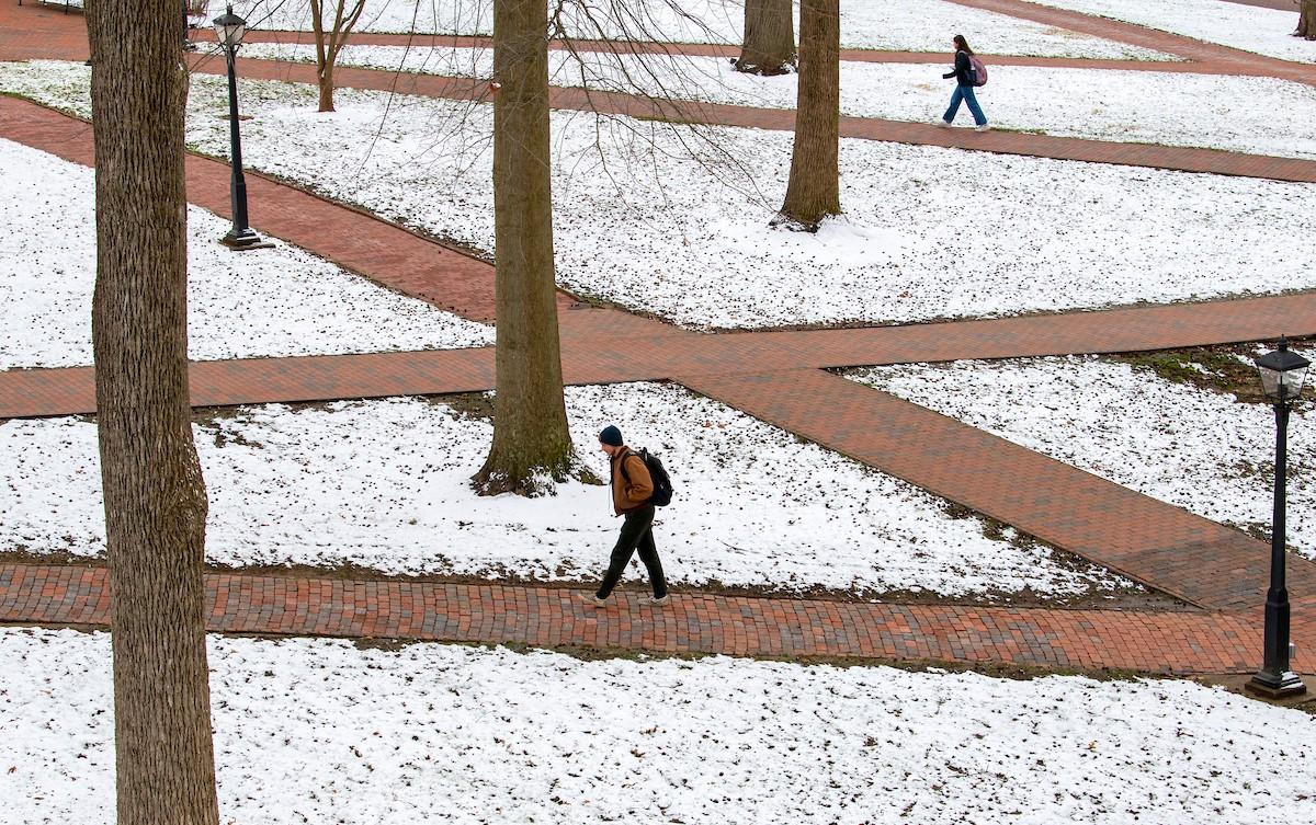 Student walking on College Green with snow on ground.