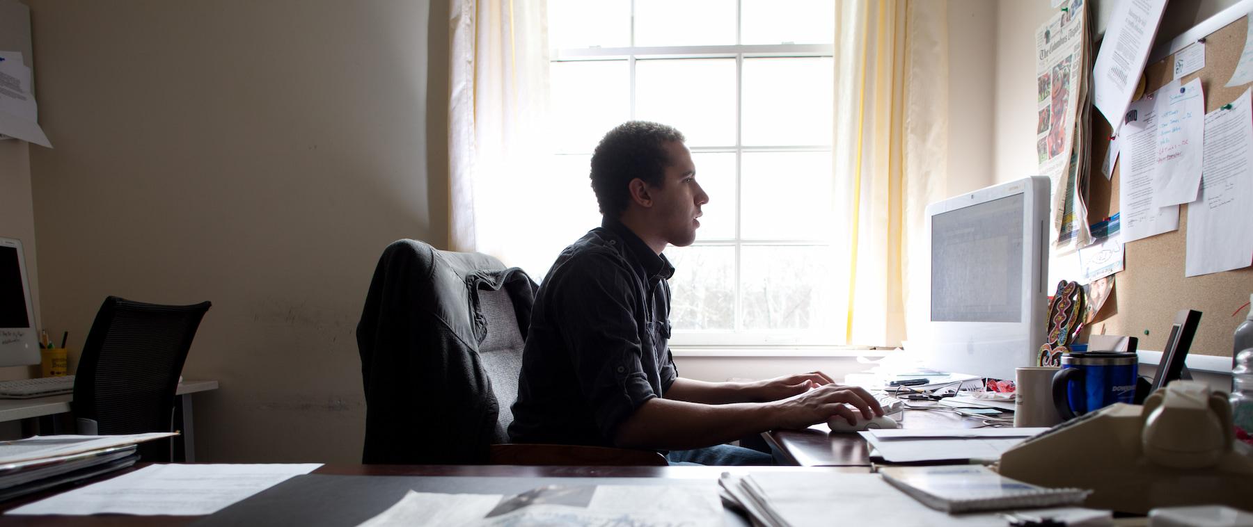 Man working on a computer while surrounded my newspapers