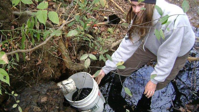 A woman holding a bucket, smiling and cleaning up septage waste in a river