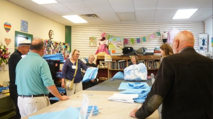 Group of people standing around large table with blue piles of blue wrap fabric.