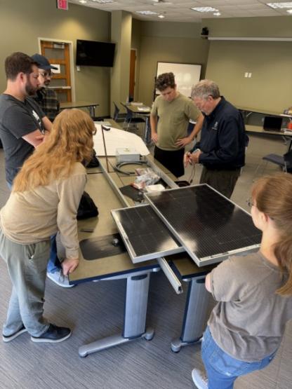 Group of people standing around table working on solar panel.