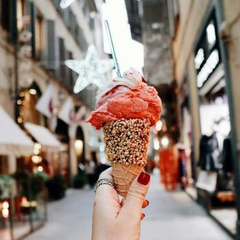 Hand holding an ice cream cone with city alley in the background.