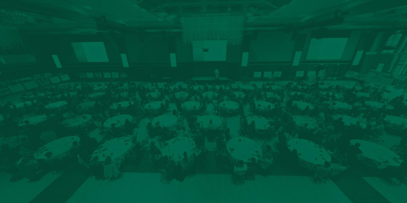 Overhead view of many round tables in front of a stage presentation